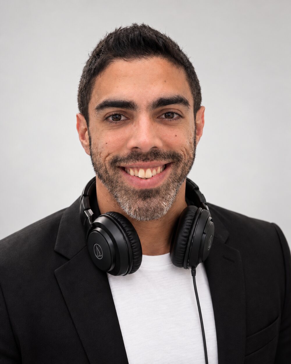 DJ Fidel headshot — smiling, headphones around his neck