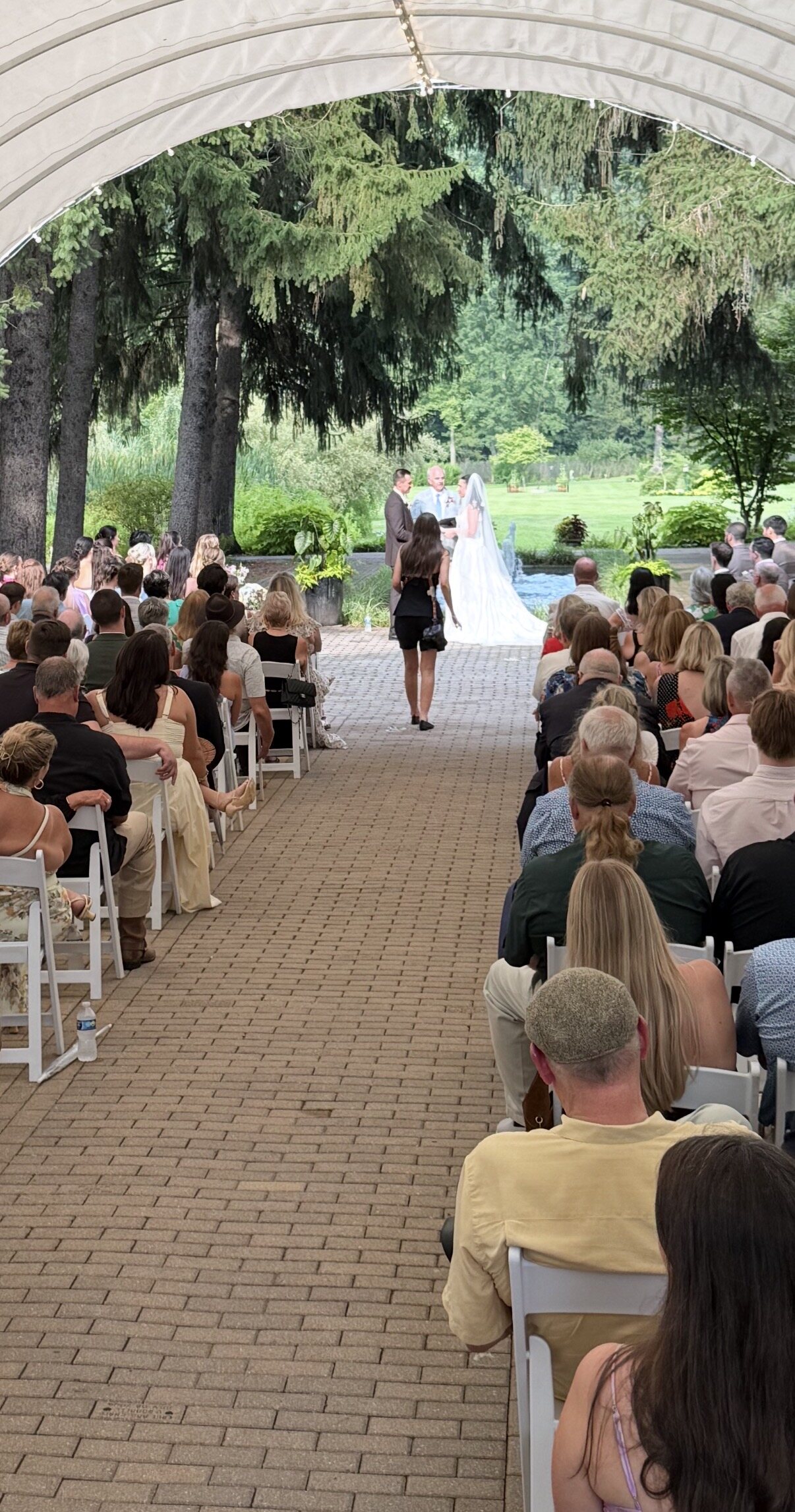 Spencer and Kit's ceremony in the Symphony Garden at Friendship Botanic Gardens, guests seated under a covered walkway leading to the greenery