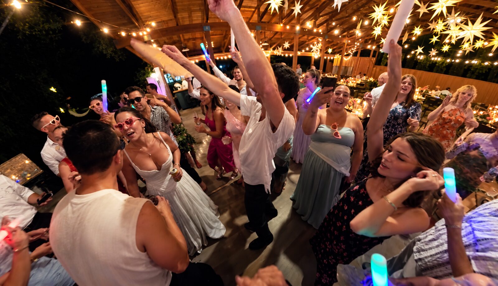 Spencer and Kit's guests dancing with glow sticks under the string lights of the reception pavilion